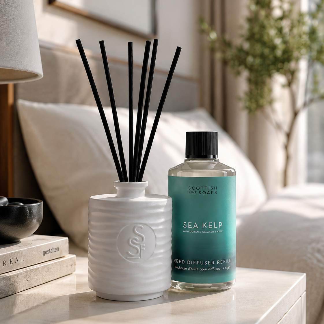 A bottle of Scottish Soaps Sea Kelp Reed Diffuser Refill next to a white ceramic diffuser jar with black reeds, styled on a bedside table in a softly lit bedroom.